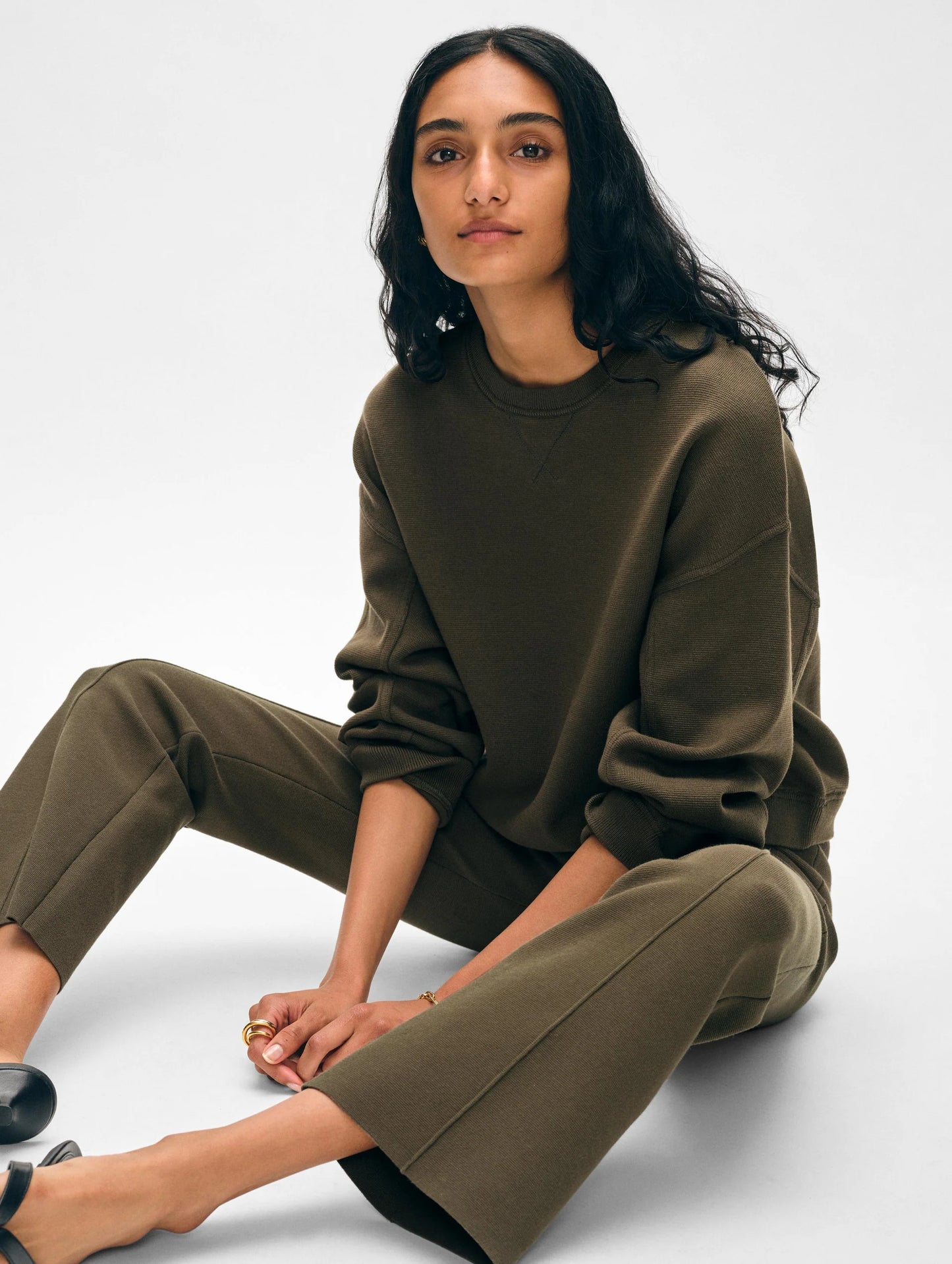 Woman sitting while wearing the Dark Sage Organic Cotton Kick Flare Pants by White + Warren