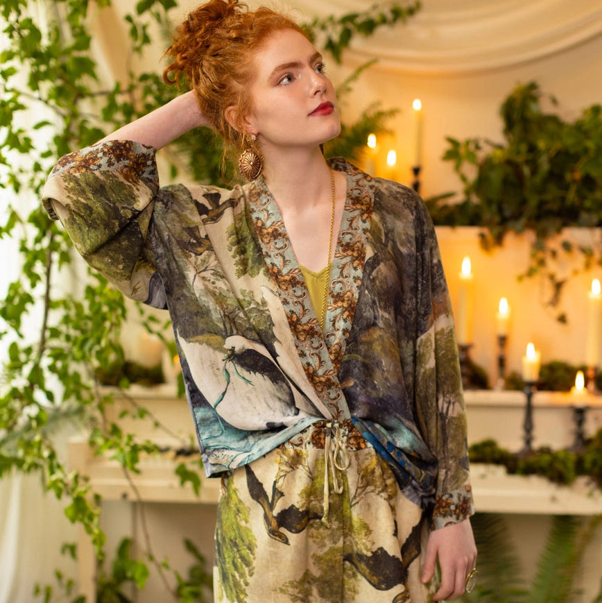Woman wearing a floral robe in a decorated room with plants and candles.