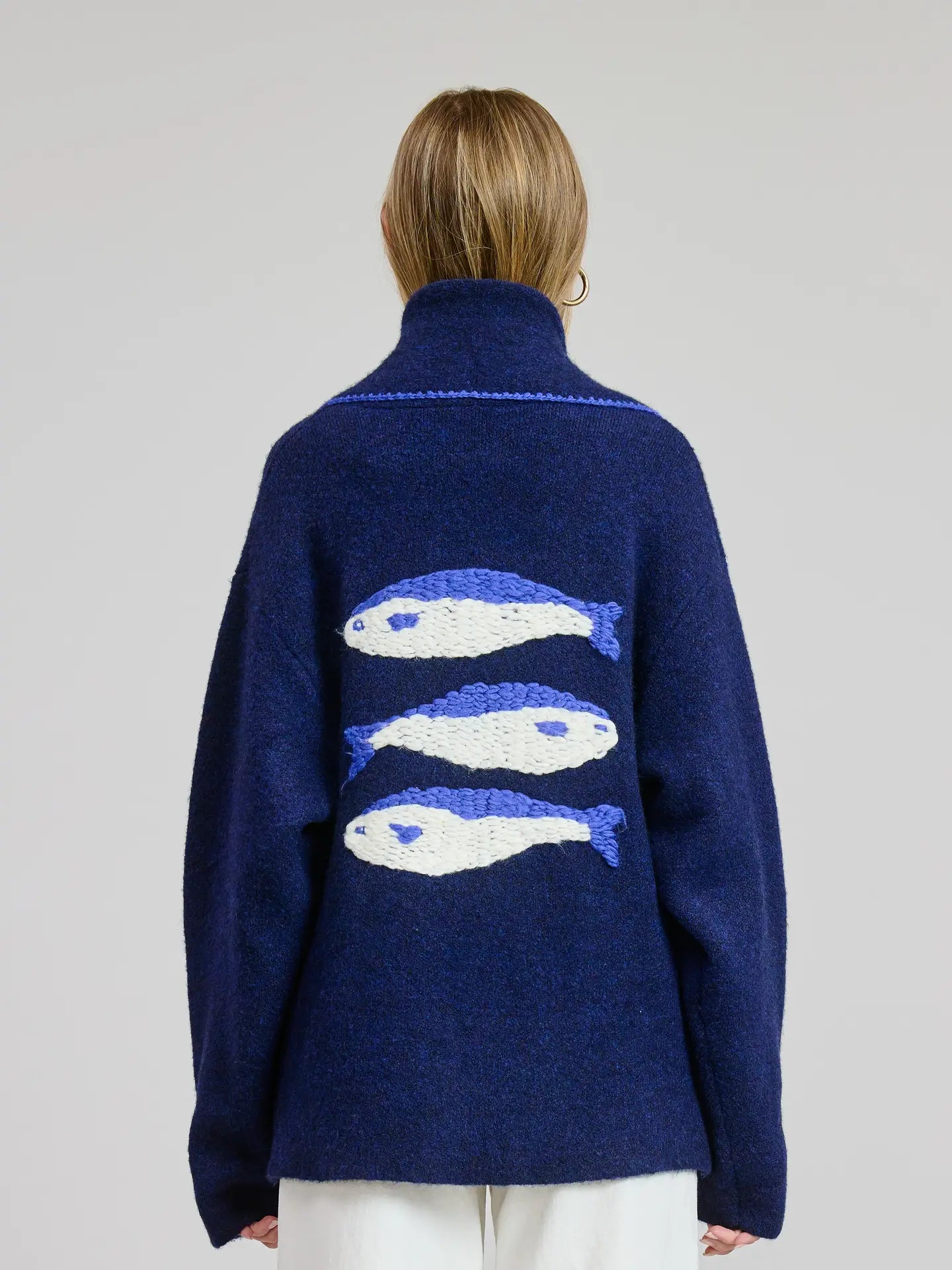 Person wearing a navy blue sweater with fish patterns on the back