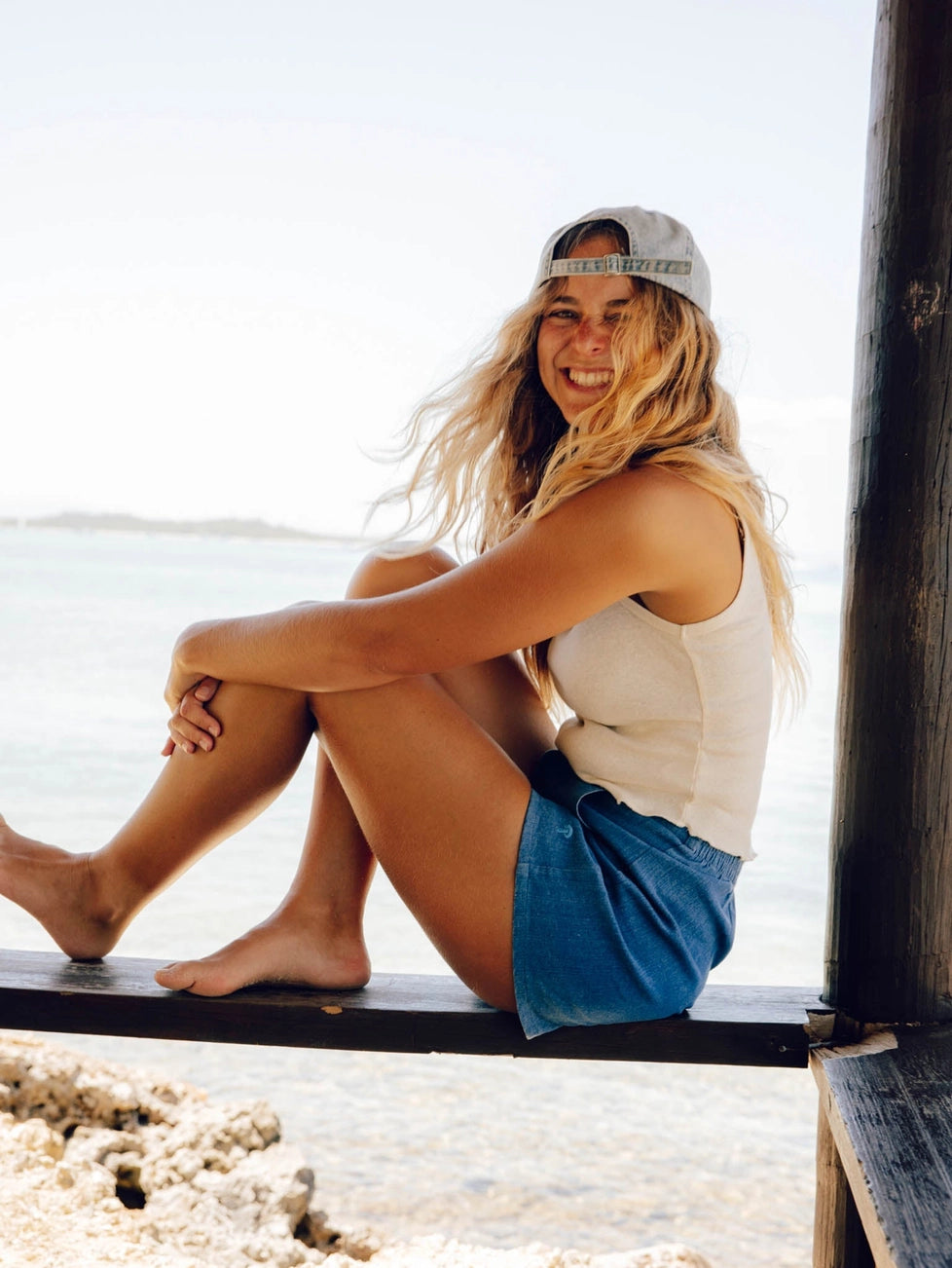Woman sitting on a wooden bench by the water, wearing the Strawberry Hat by Mollusk