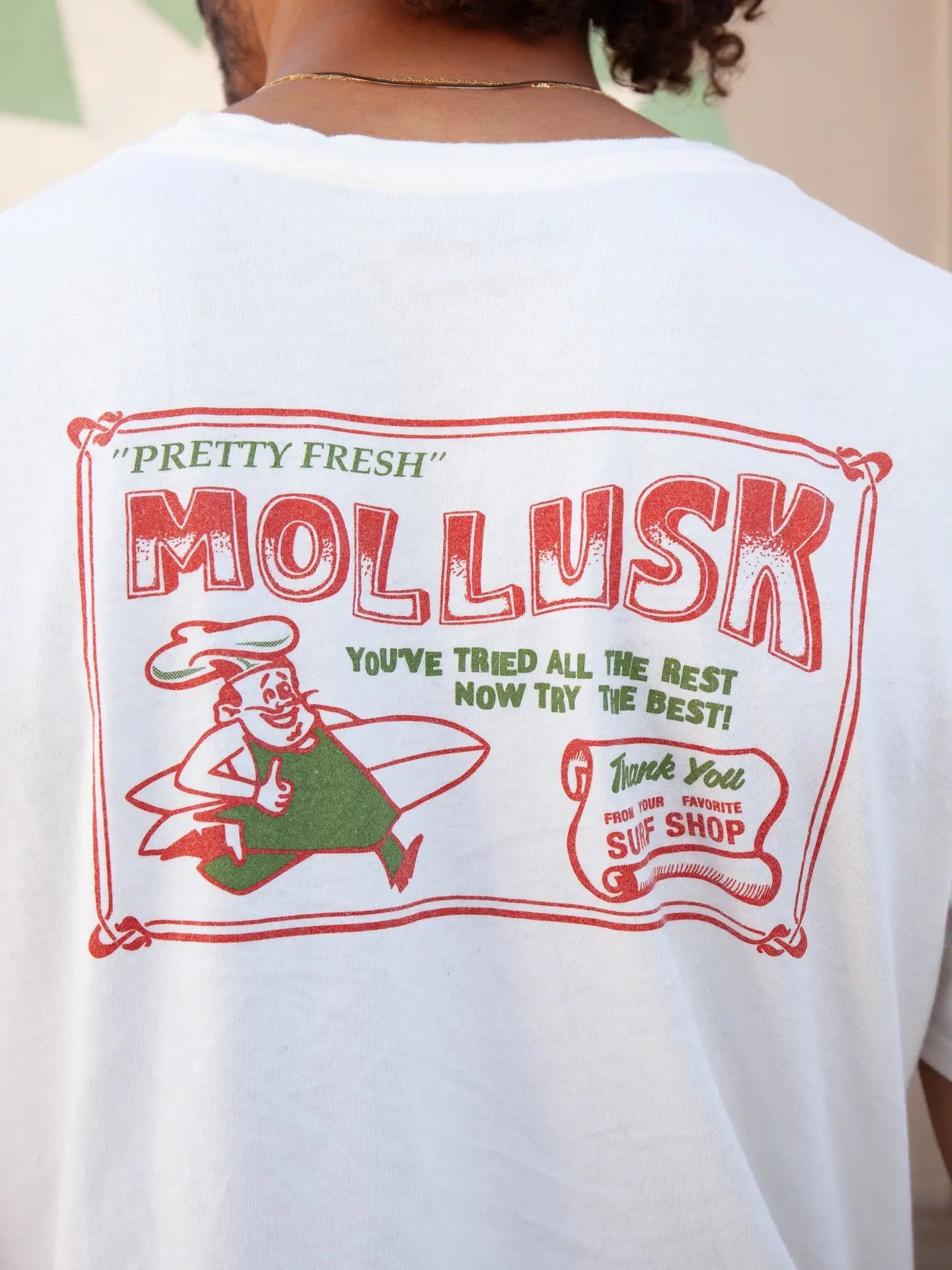 White t-shirt with red and green graphic design on the back, featuring the text 'Pretty Fresh Mollusk' and a cartoon character.