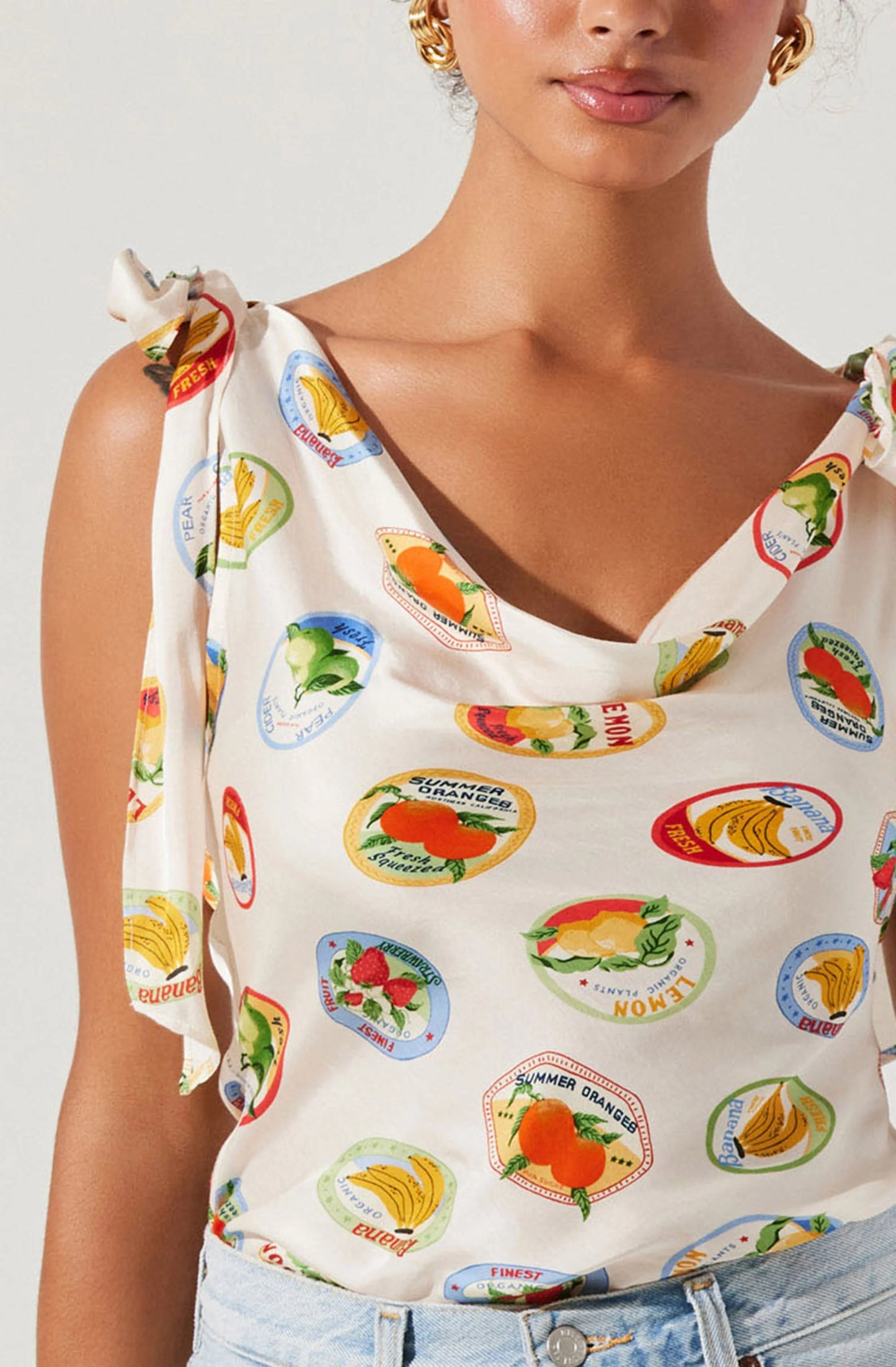 Woman wearing a sleeveless top with colorful fruit and vegetable prints on a plain background
