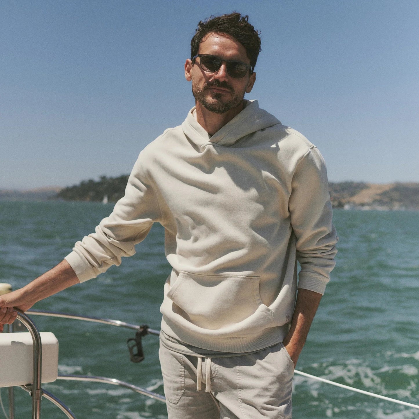 A man wearing the white Cloud 9 Fleece Relaxed Hoodie by Marine Layer on a boat
