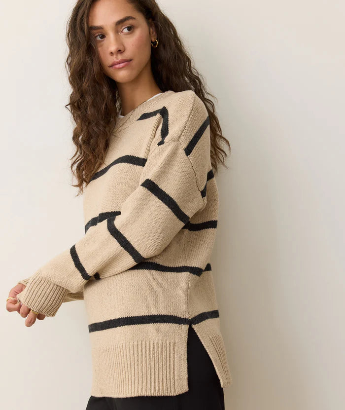 Woman wearing a beige sweater with black stripes against a plain background