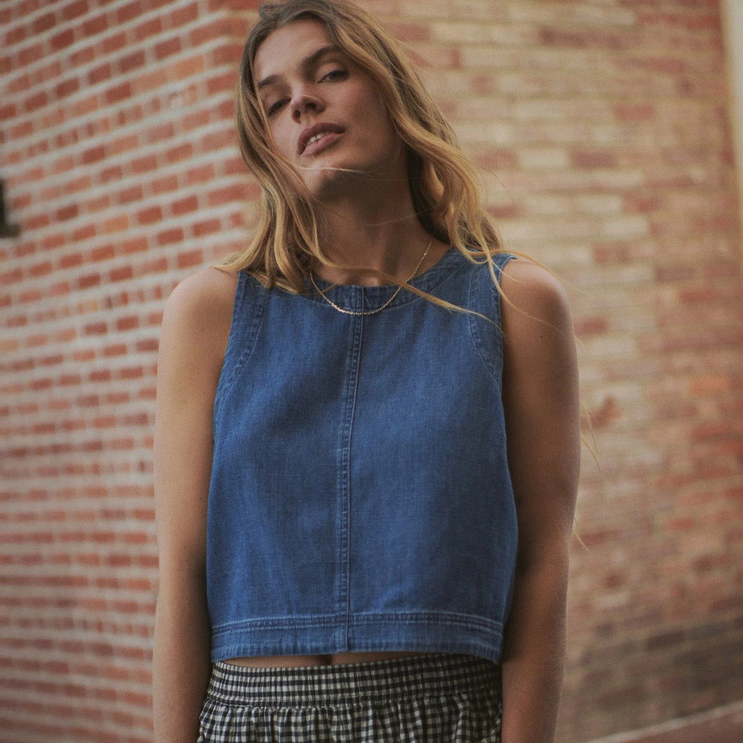 A woman wearing the Marine Layer Quinn Denim Tank in front of a brick wall
