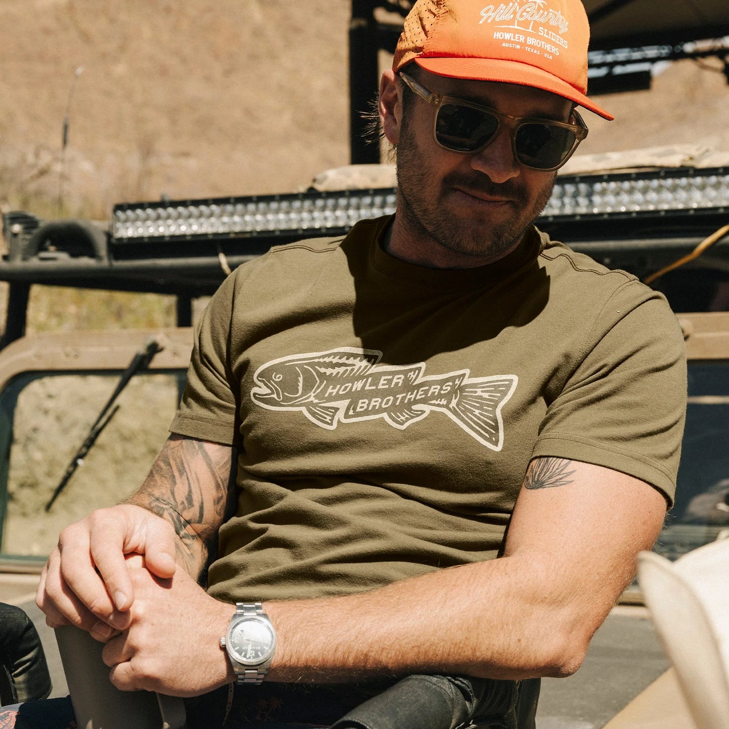 Man wearing an orange cap and green t-shirt with a fish graphic, sitting outdoors.