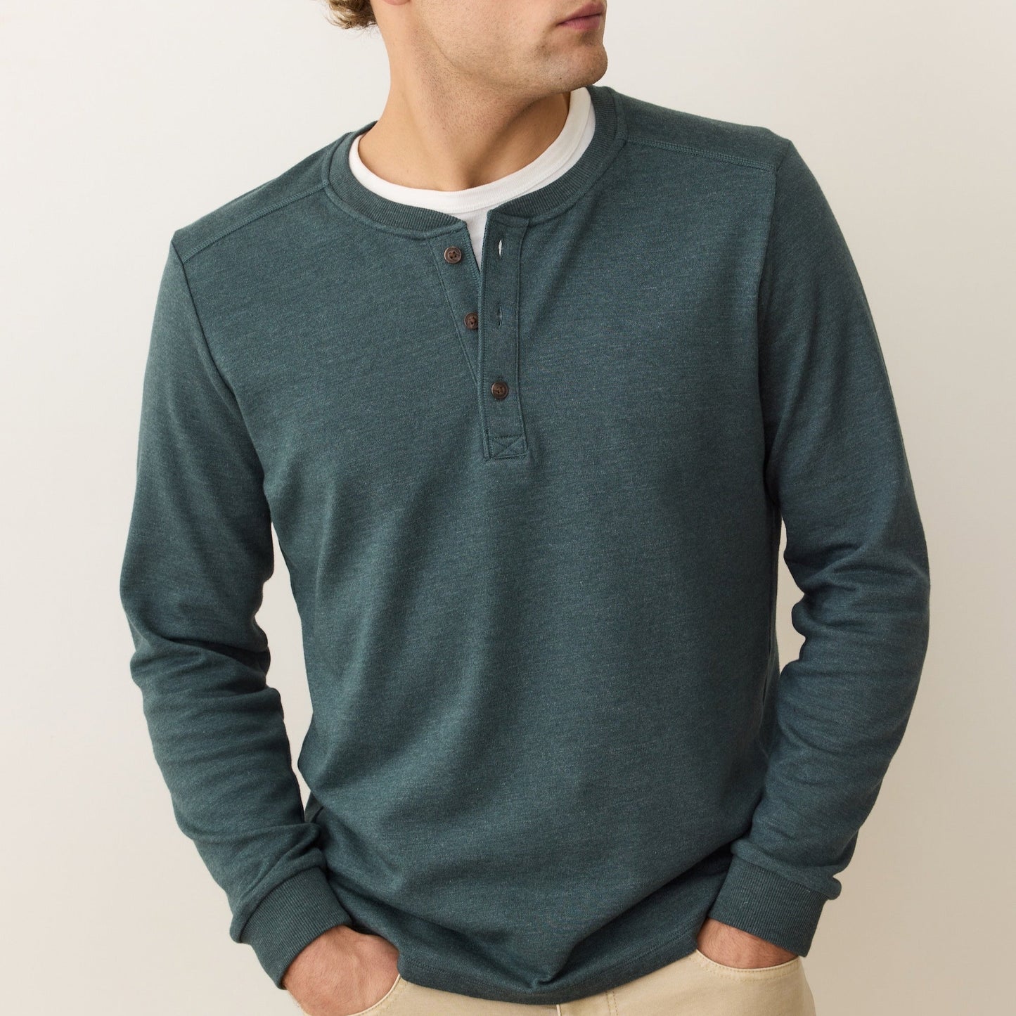 A man wearing the Marine Layer Pacifica Stretch Henley in the color Green Gables layered over a white t-shirt
