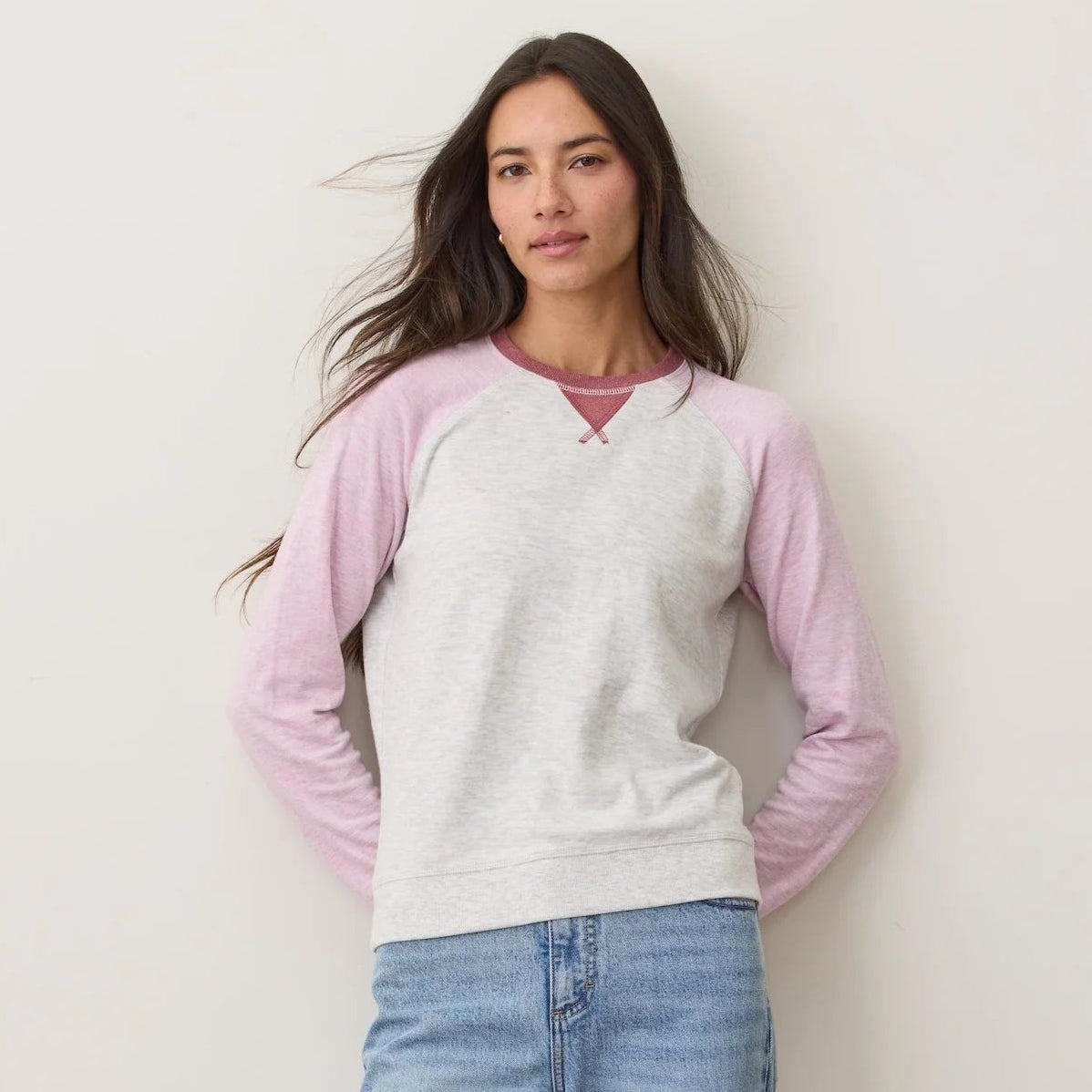 Woman wearing the The Marine Layer Varsity Raglan leaning against a plain wall.