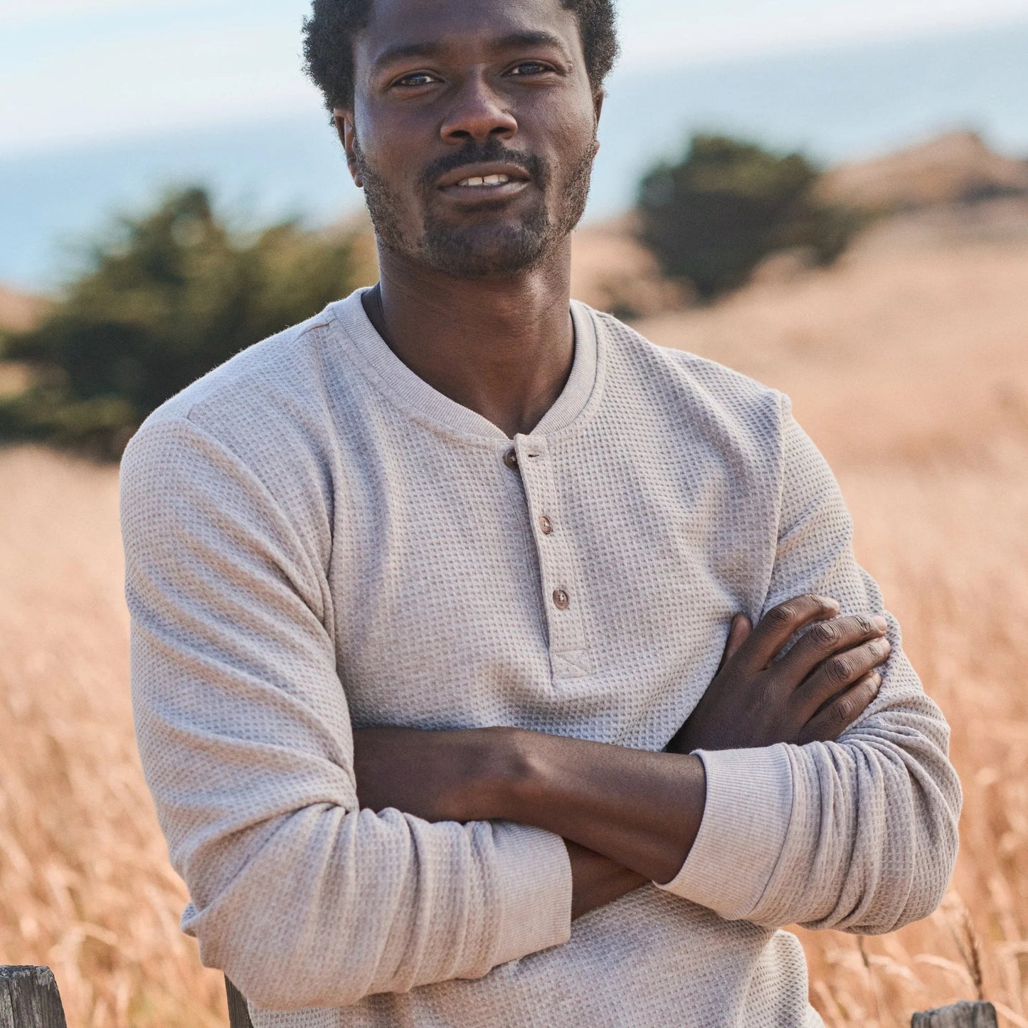 Man wearing a beige long-sleeve waffle henley shirt standing in a field
