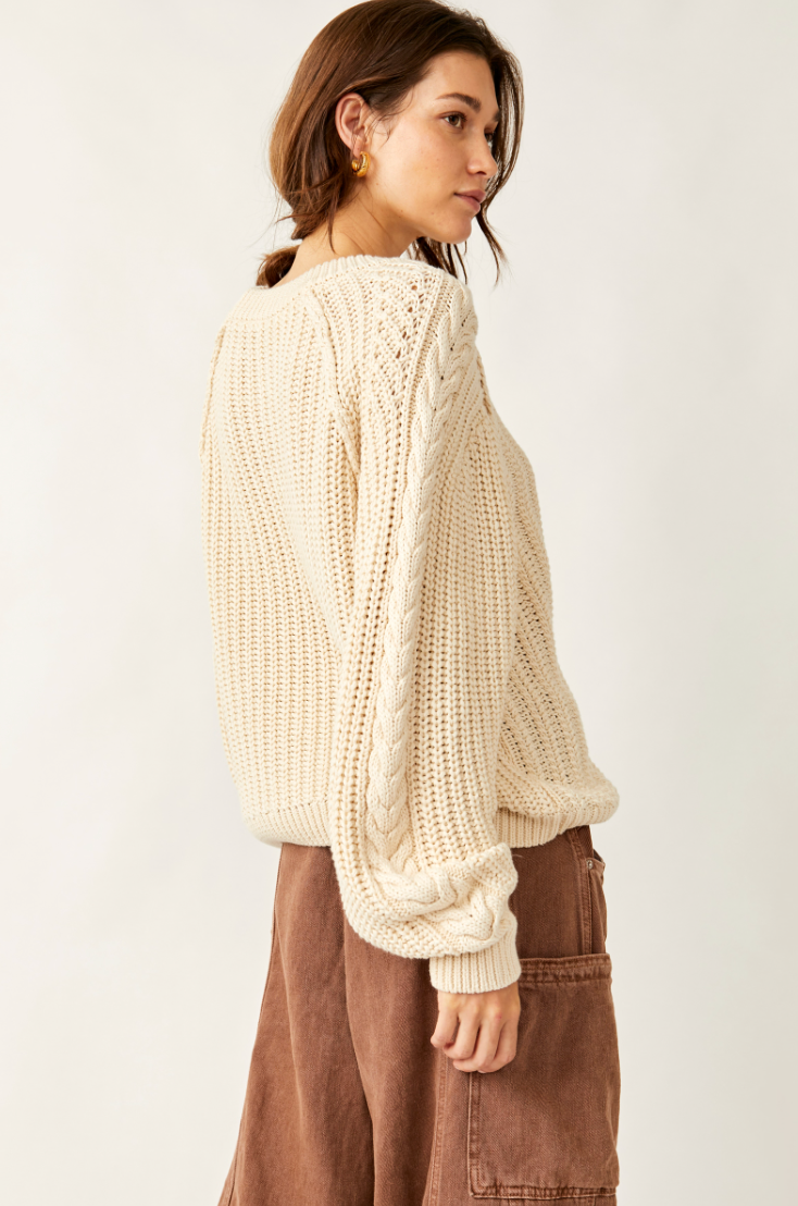 Woman wearing a cream knitted sweater and brown pants on a white background