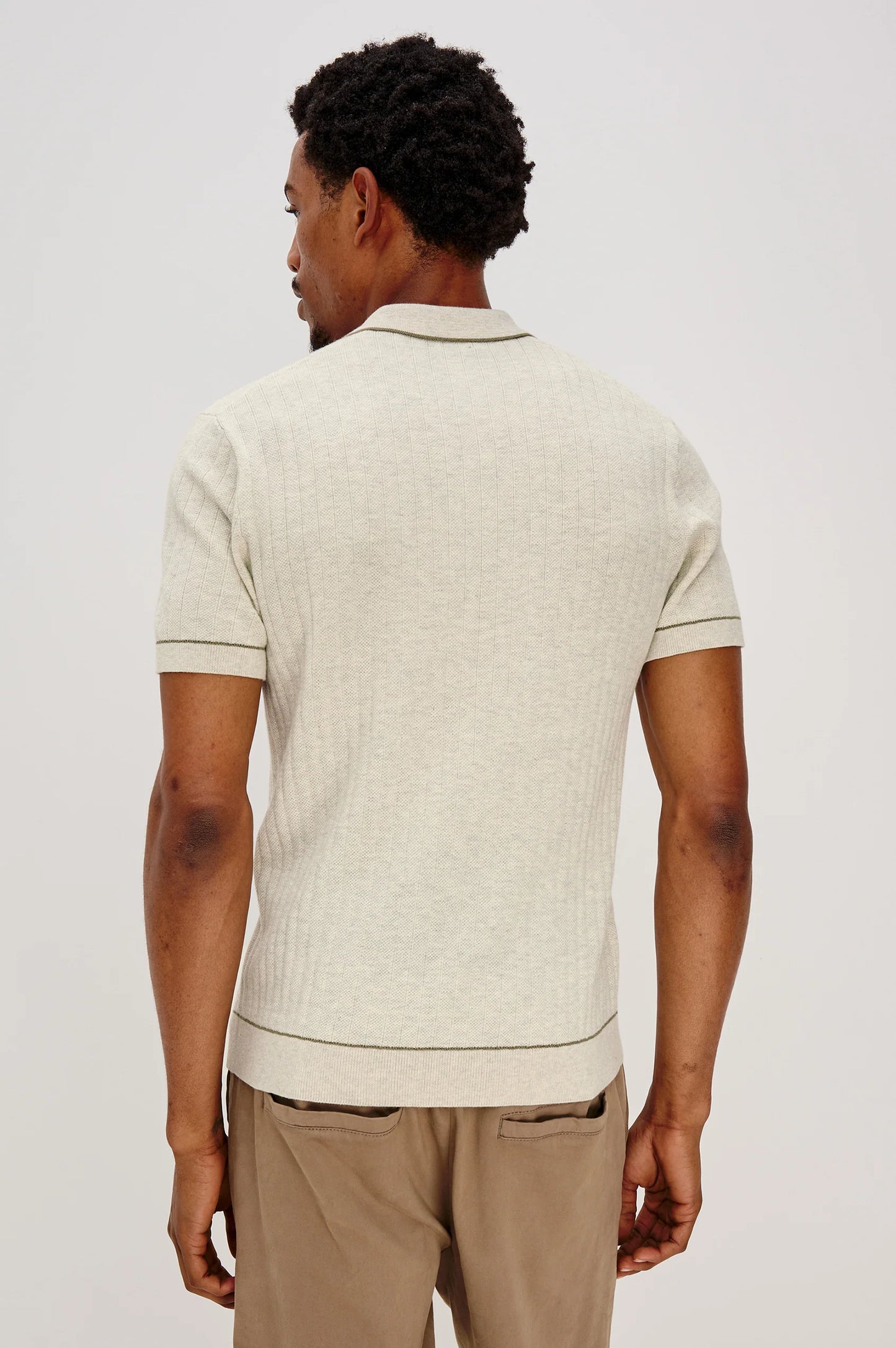 Man wearing a beige patterned polo shirt and beige pants on a white background