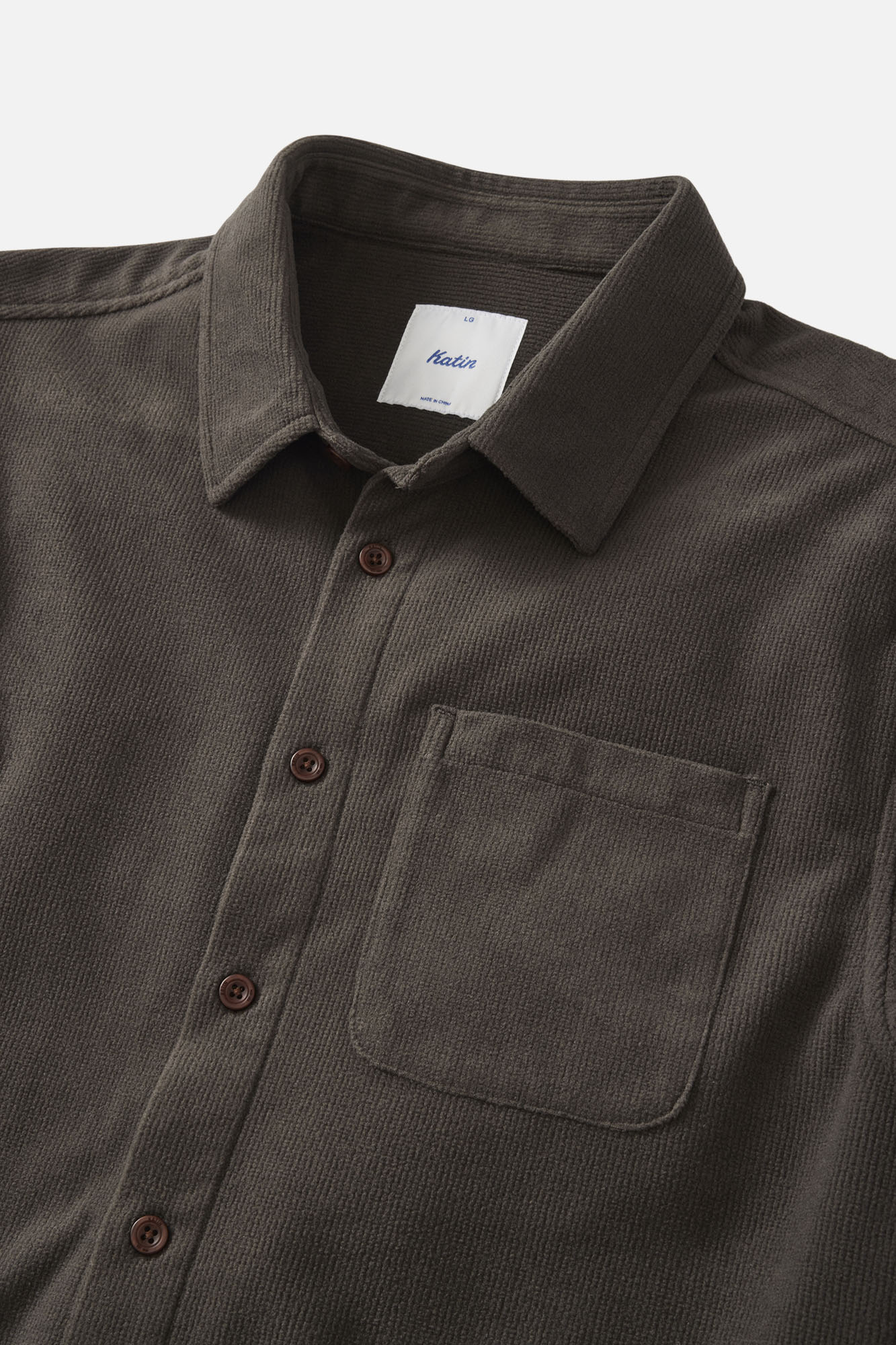 Dark brown corduroy shirt with collar and pocket on a light gray background