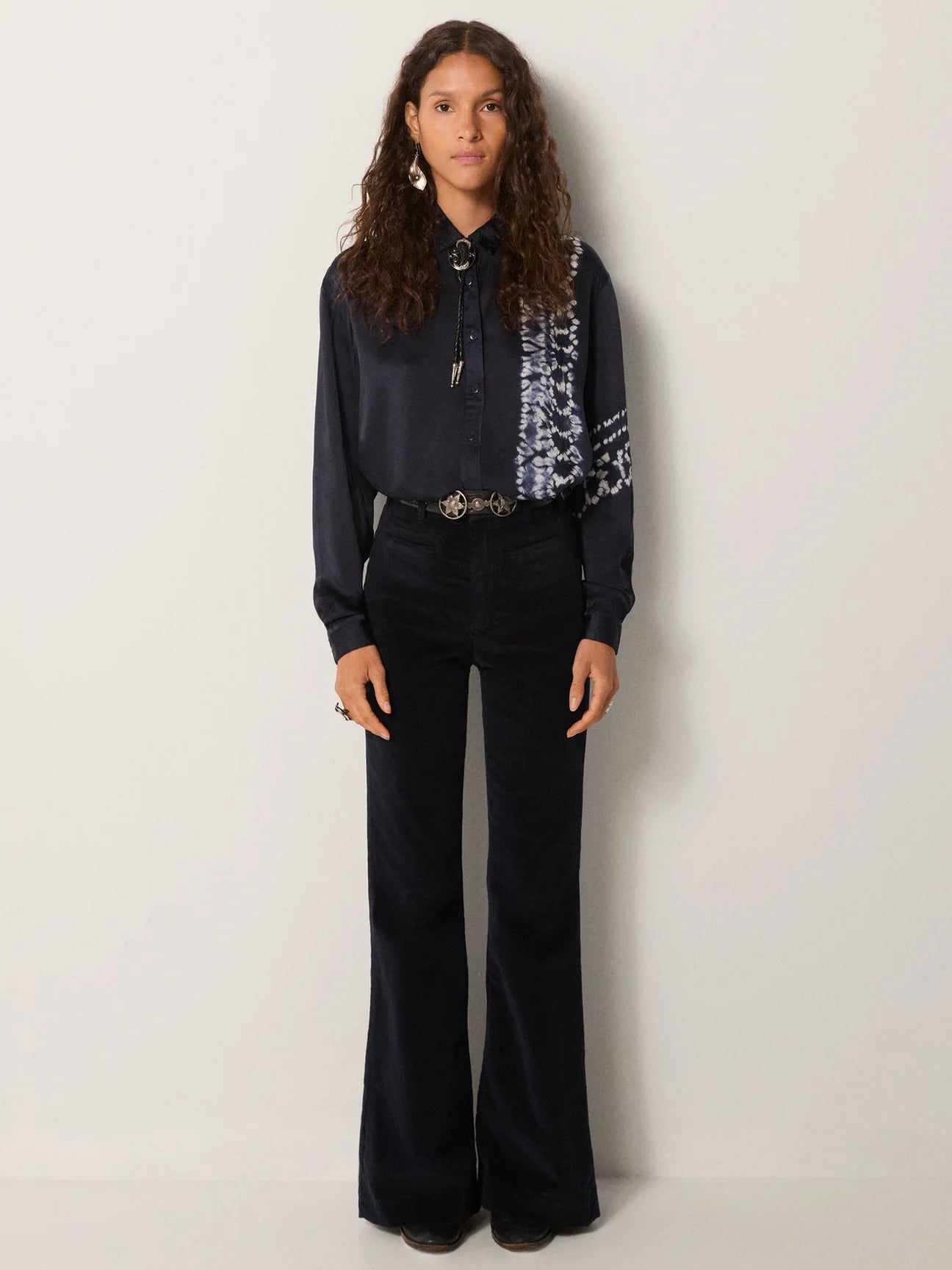 A woman wearing the Maison Hotel Elizabeth Blouse styled with a bolo and slim flare pants