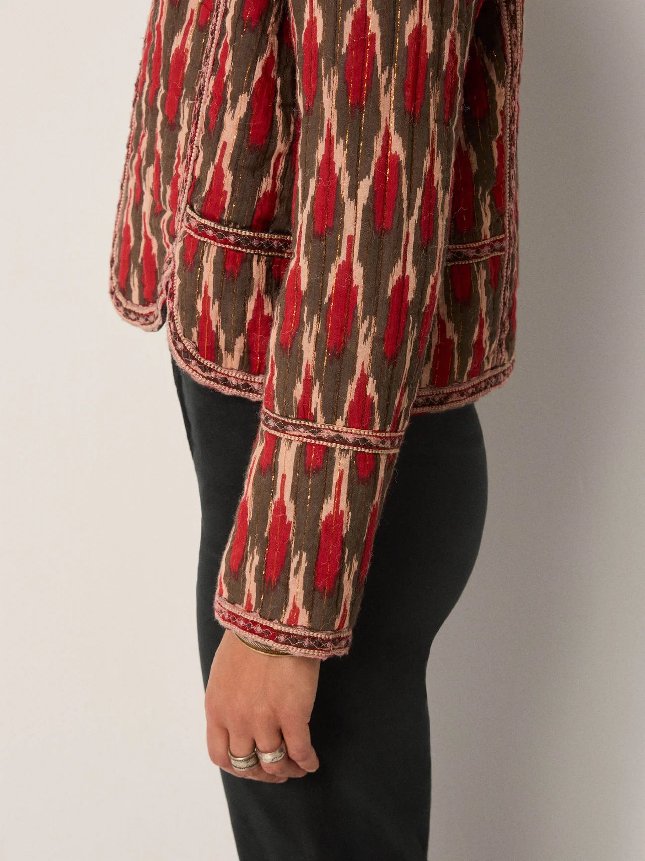 Person wearing a patterned jacket with an artful red and brown design and embroidery along the piping