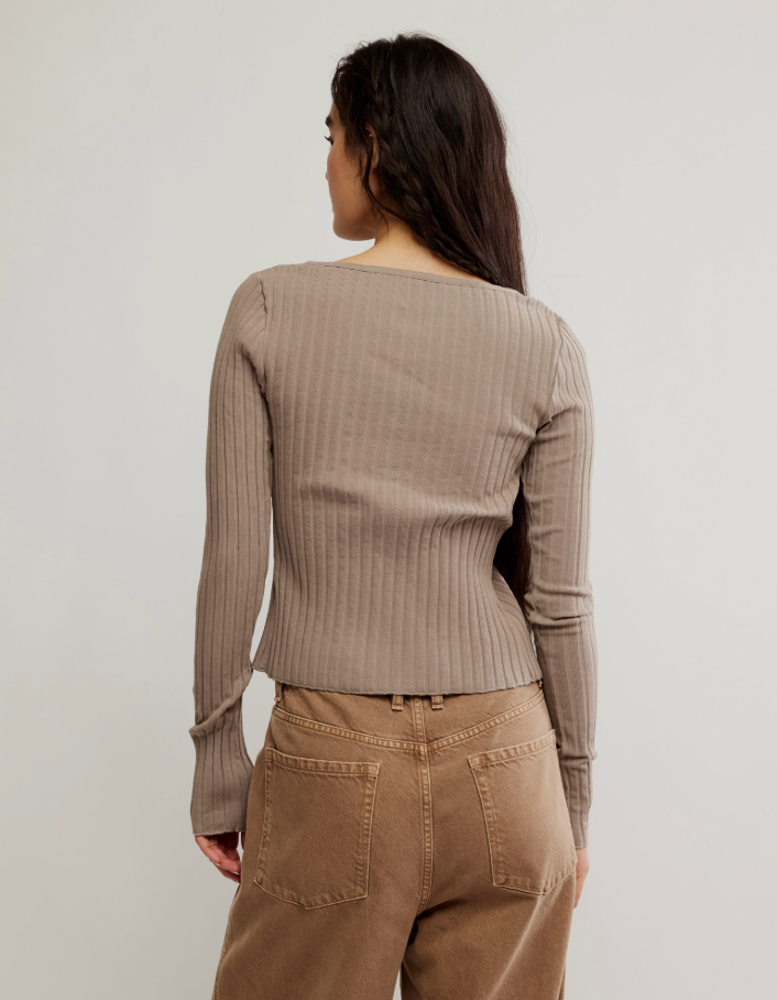 Woman wearing a beige ribbed sweater and pants against a plain background