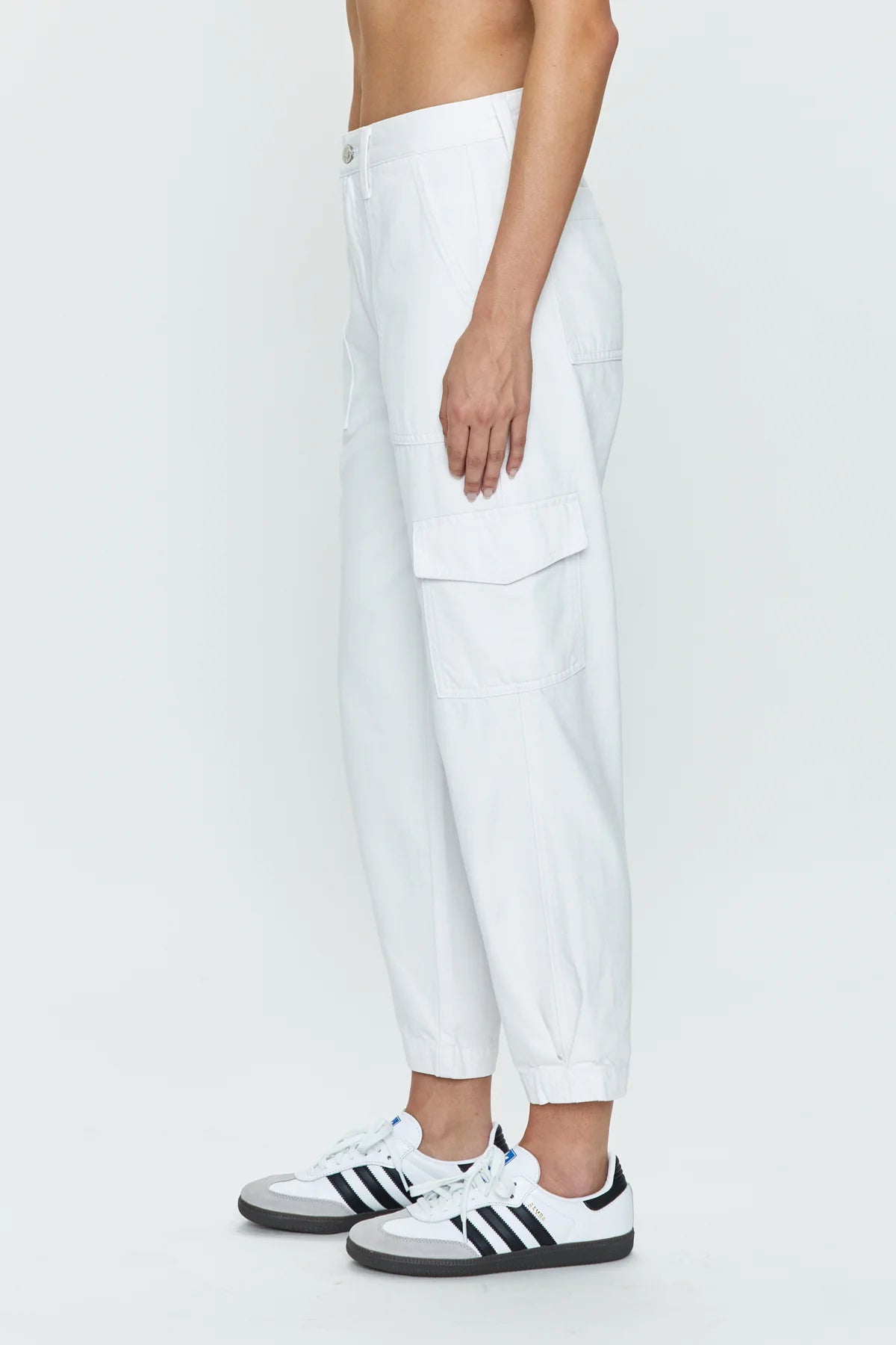 Side view of woman wearing sleek white cargo pants with a high rise and tapered ankle hem