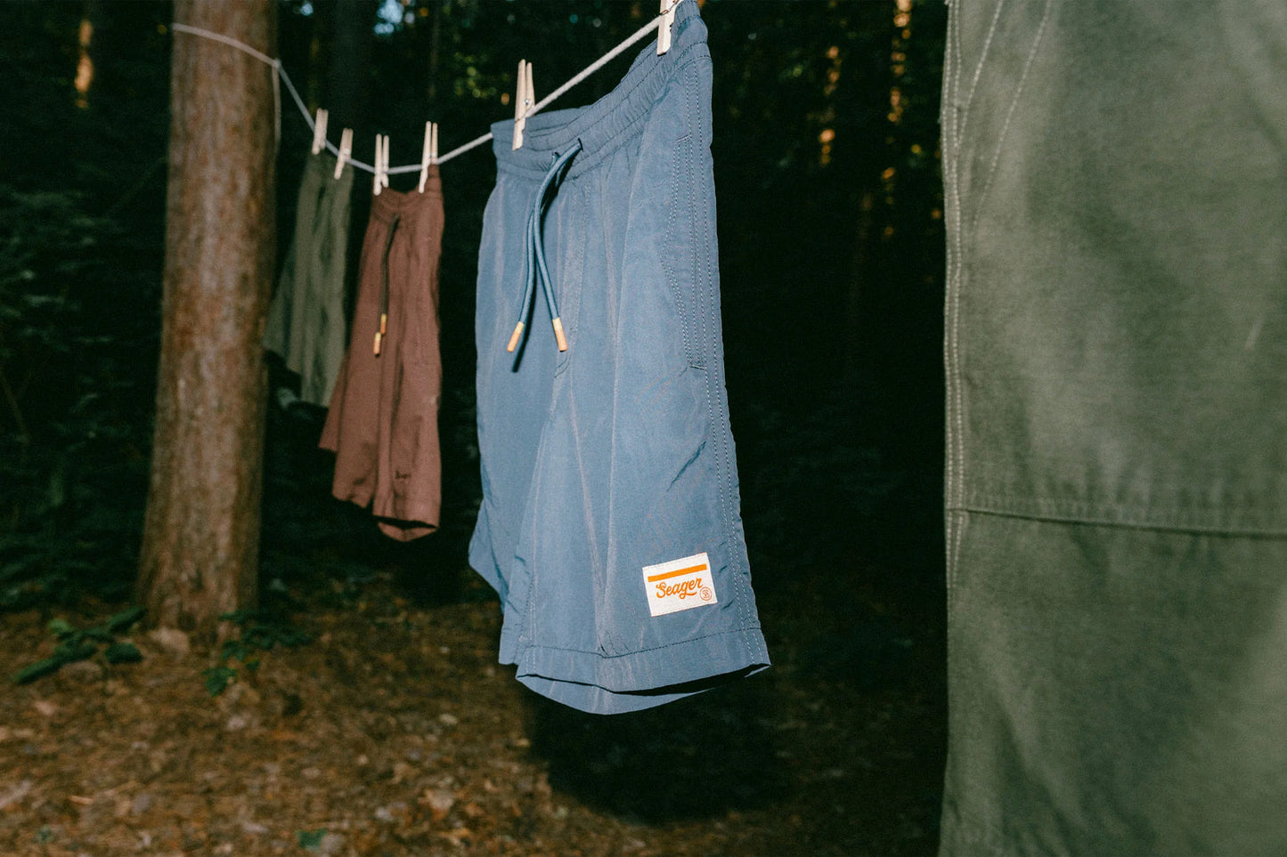 The Navy Yuma Light Shorts by the brand Seager hanging on a clothes line outdoors along with other pairs of shorts