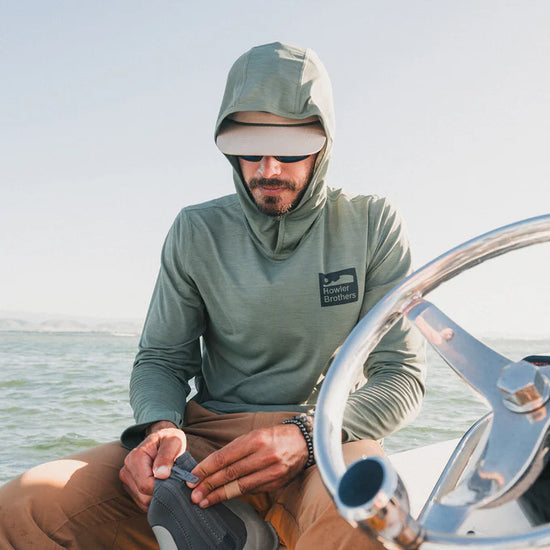 Man on a boat wearing the Howler Bros HB Tech Hoodie in the color Agave