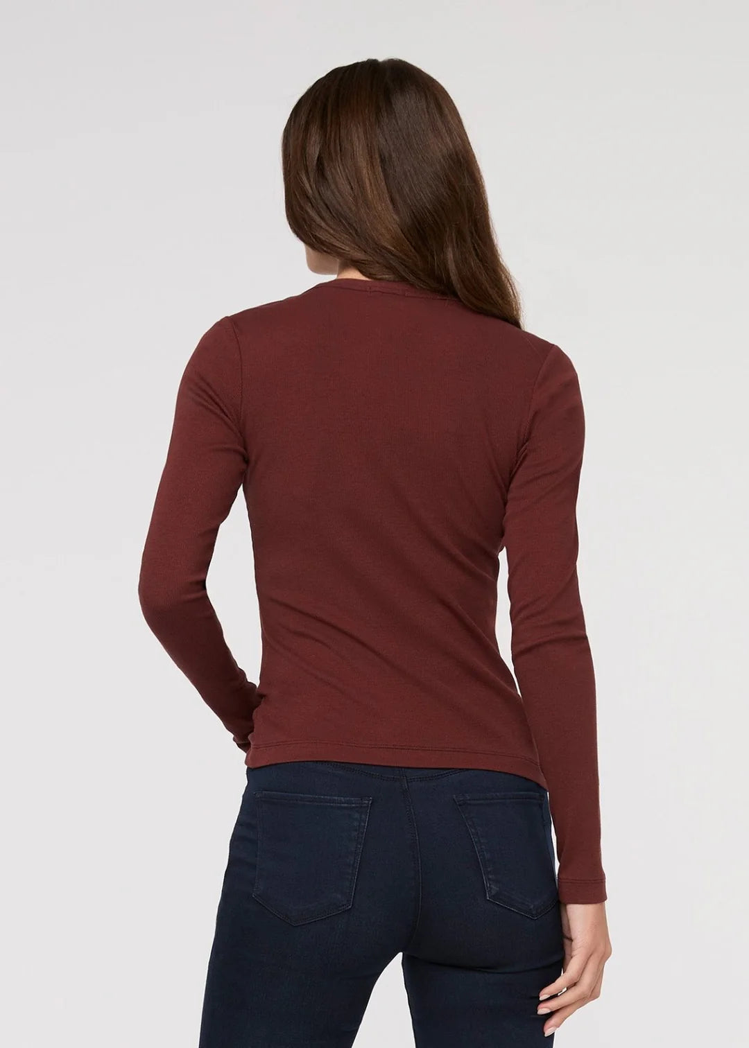 Person wearing a maroon long-sleeve shirt and dark jeans on a white background