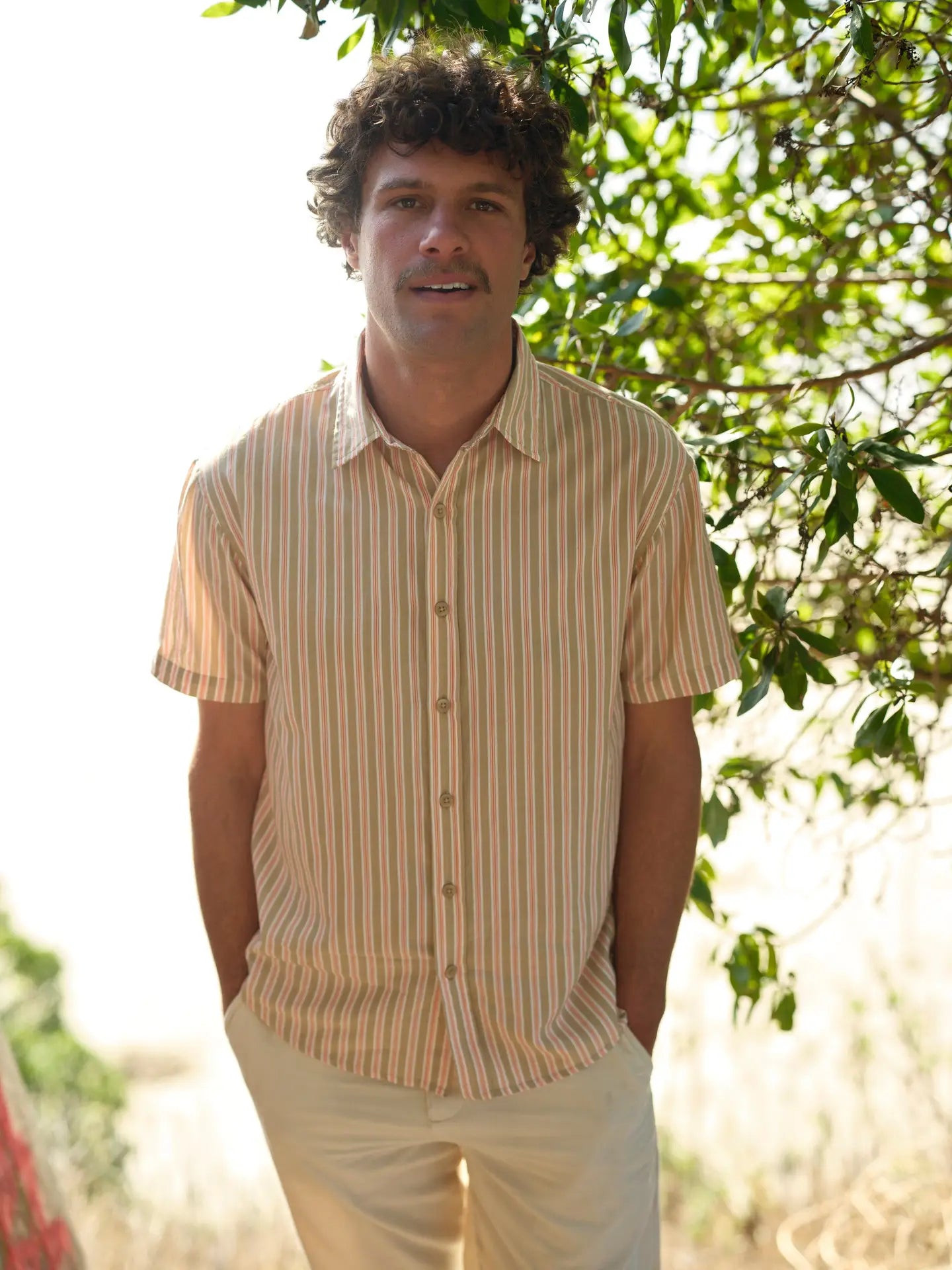 A man wearing the Mollusk Summer Shirt in Tan and Red Stripe