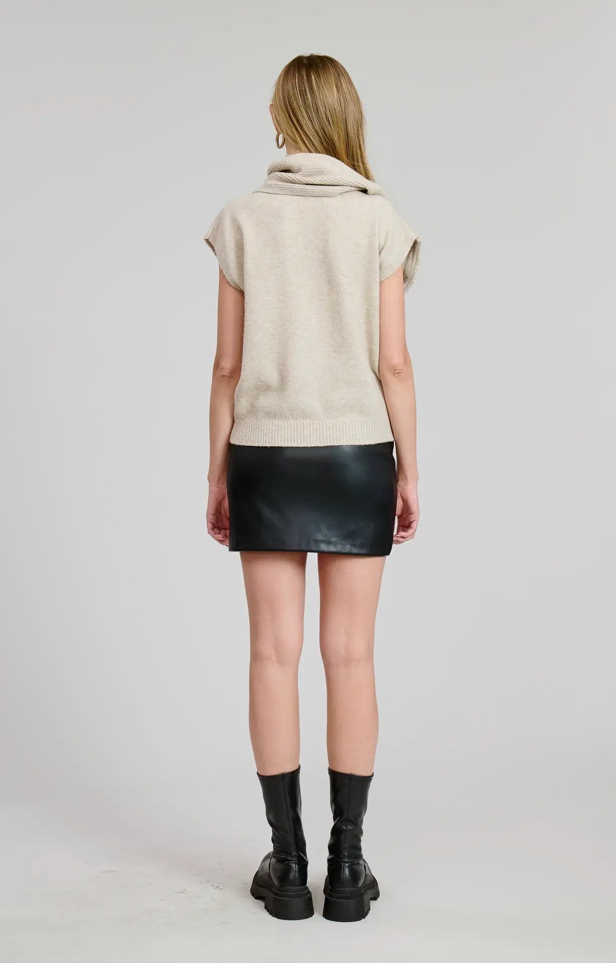 Person wearing a beige short sleeve sweater top with attached scarf detail, black leather skirt, and black boots