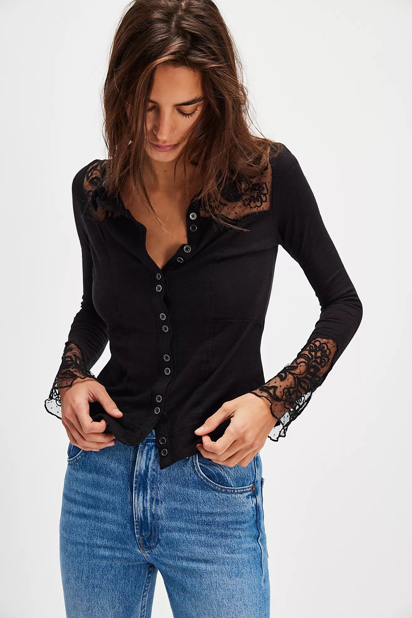 Woman wearing a black long-sleeve top with lace details and blue jeans on a white background