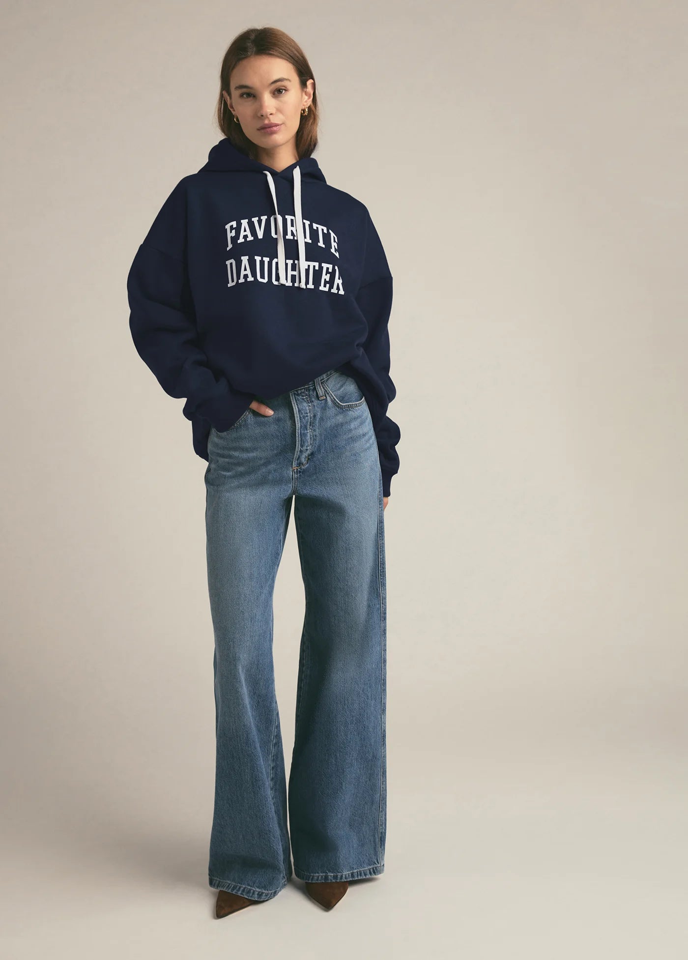 Person wearing a navy hoodie with 'FAVOURITE DAUGHTER' text and blue jeans on a beige background