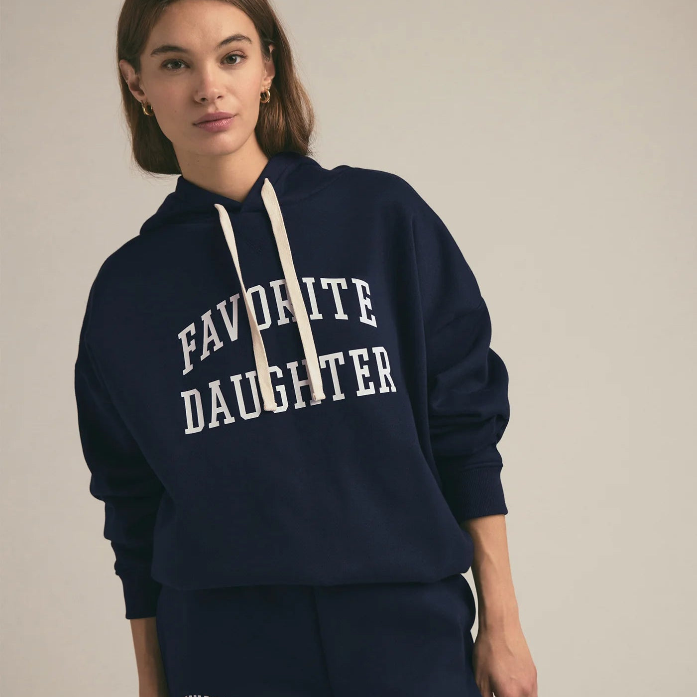 Woman wearing a navy hoodie with 'FAVORITE DAUGHTER' text on a plain background