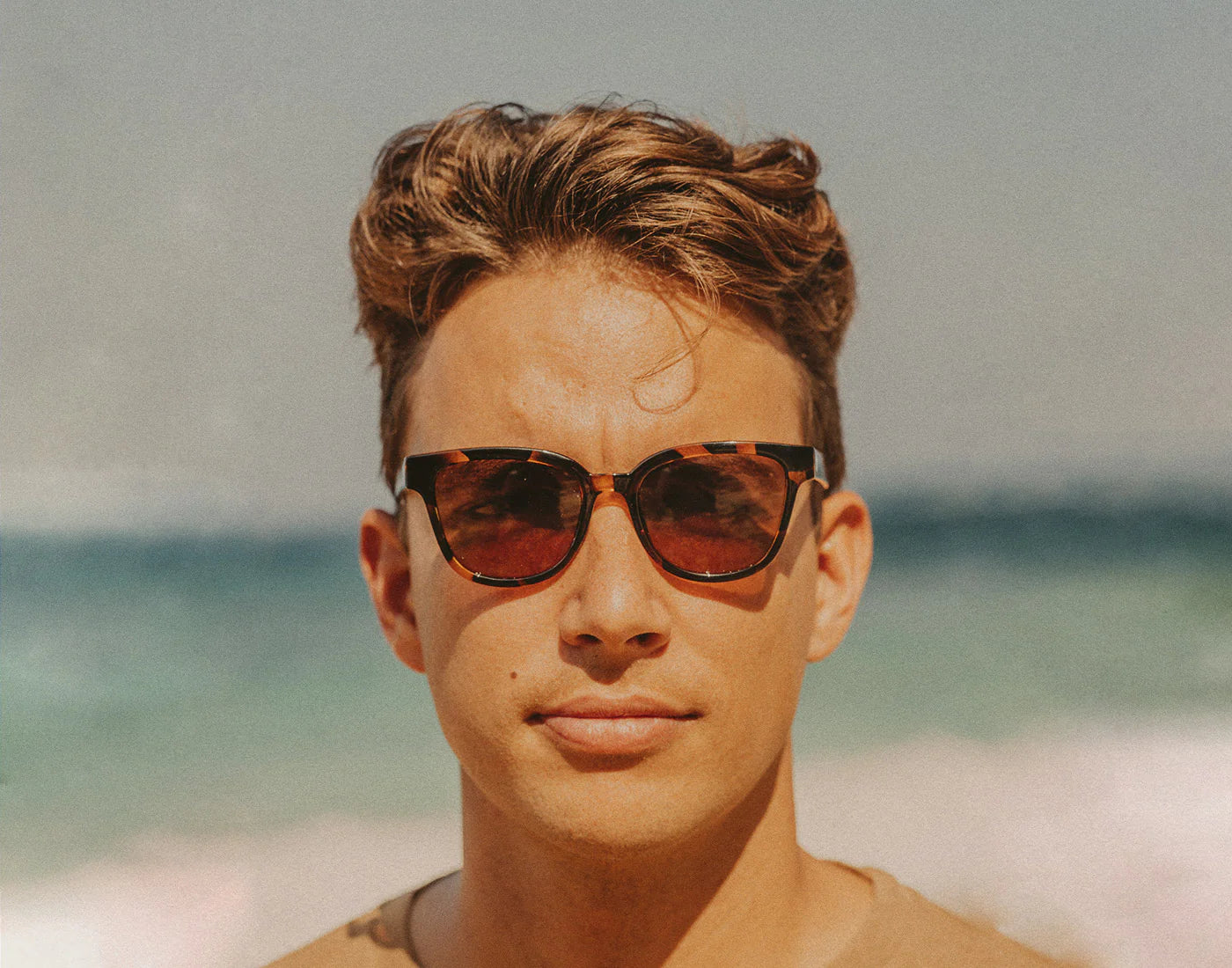 Man wearing the Sunski Miho sunglasses in Tortoise Amber with a beach background