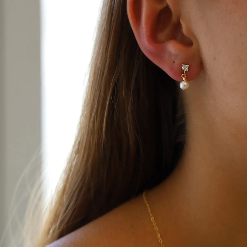 Close-up of a person wearing pearl and cz square stone earrings.