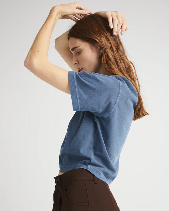 Side view of a woman wearing a relaxed fit short sleeve cropped t-shirt in a mid-blue color called moonlit ocean