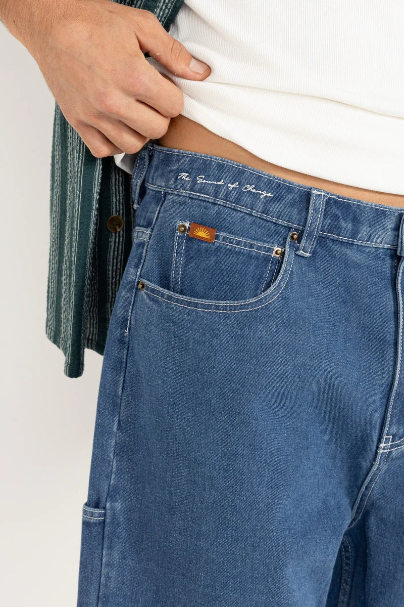 Close-up of dark blue wash men's denim shorts with a Rhythm logo