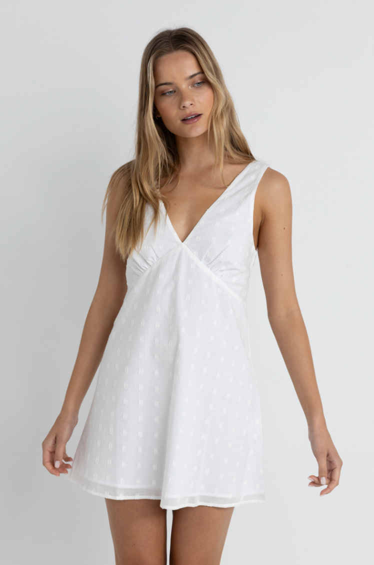 The Rhythm Mirage Mini Dress is available a Harbour Thread in the color White, and features a v-neckline with gathering under the bust. 