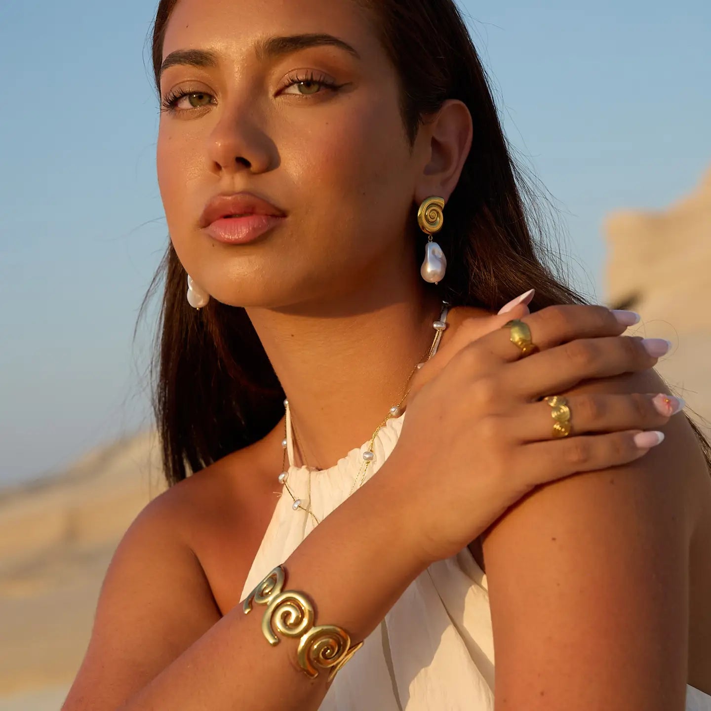 Woman wearing gold and pearl jewelry with a desert background