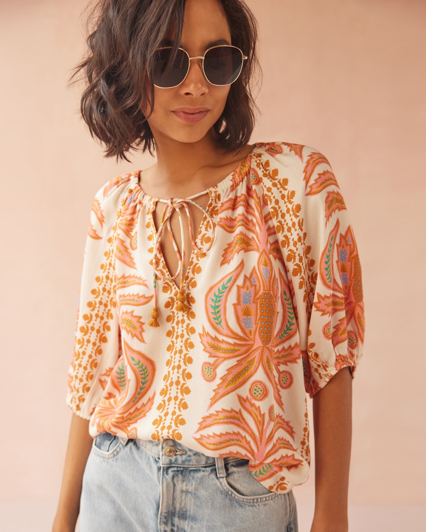 A woman wearing the Zena Sunrise Isla Blouse from OMIKA, paired with sunglasses and jeans