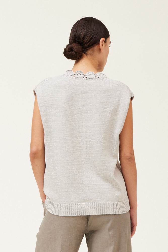 Back view of a woman wearing a sleeveless crochet trim sweater top 