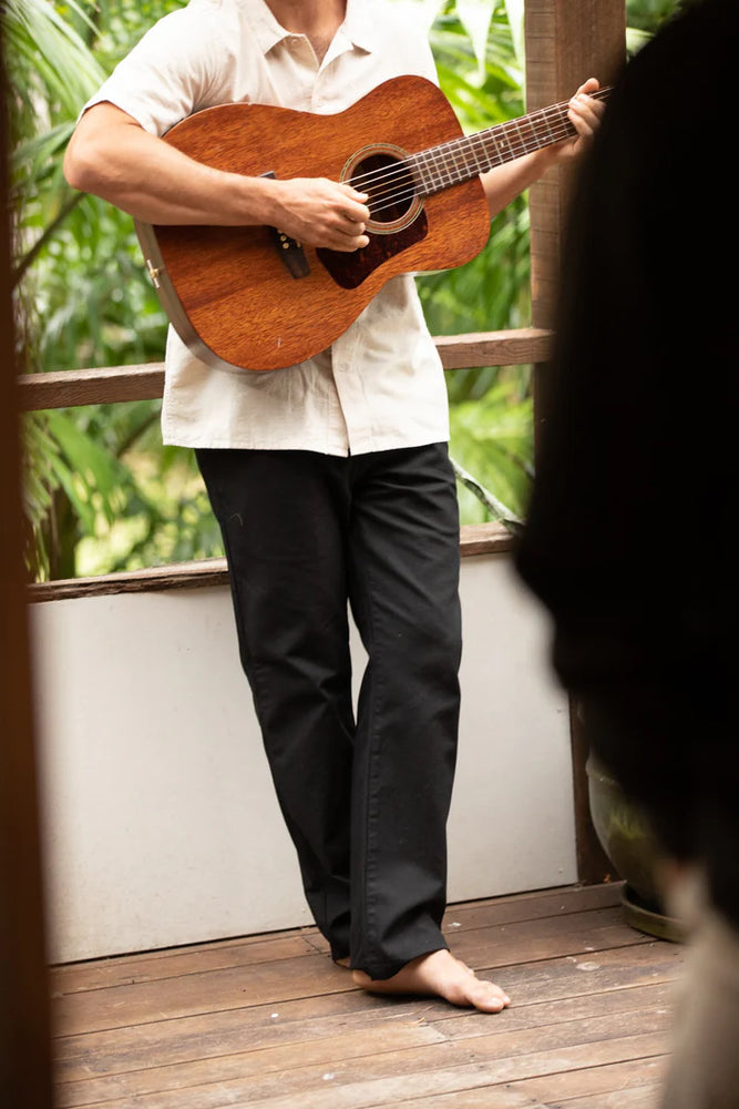 A man wearing the Vintage Black Classic Fatigue Twill Pants by Rhythm while playing the guitar