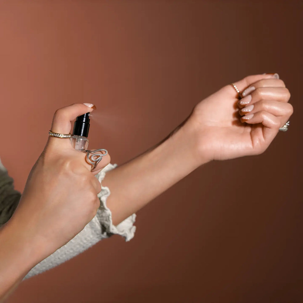 Person spraying perfume on their wrist against a brown background