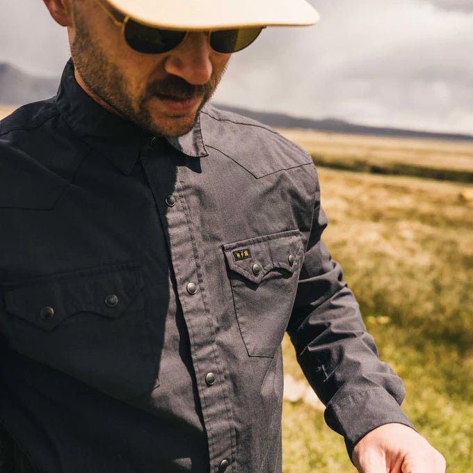 closeup lifestyle photo of man wearing a dark grey, western-style snap button up shirt