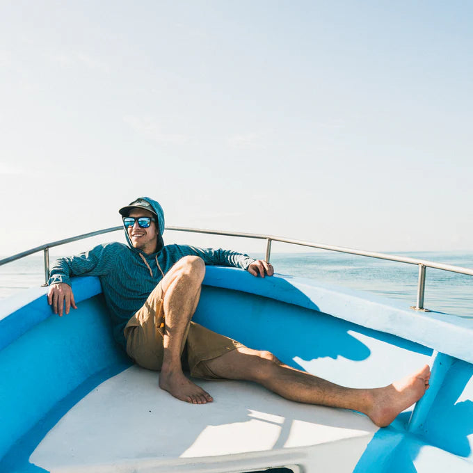 A man on a boat wearing the Deluge Camo Pacific Blue Loggerhead Hoodie by Howler Brothers