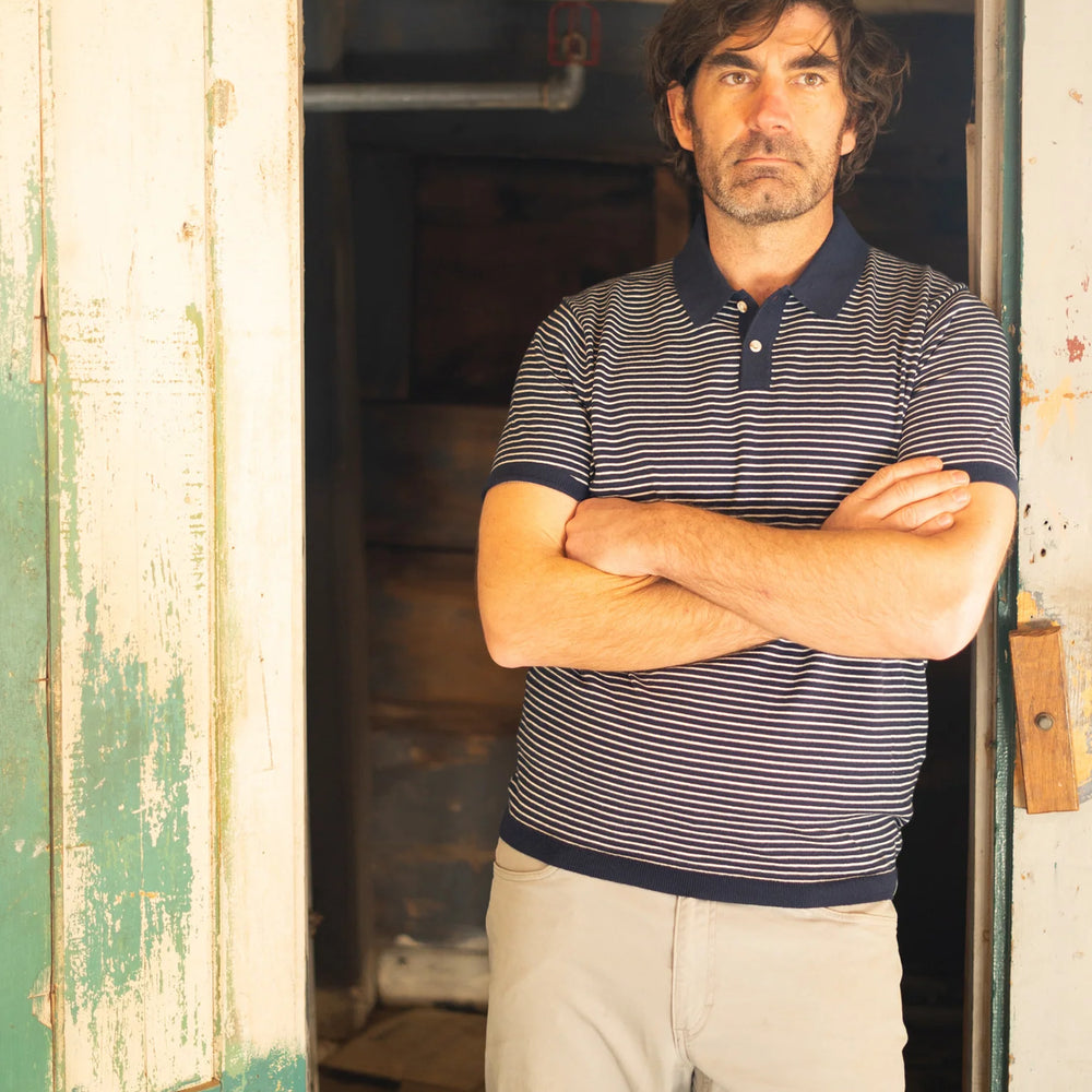 
                      
                        A man standing in a doorway while wearing the Navy SeaWell Striped Knit Polo by Long Wharf Supply
                      
                    