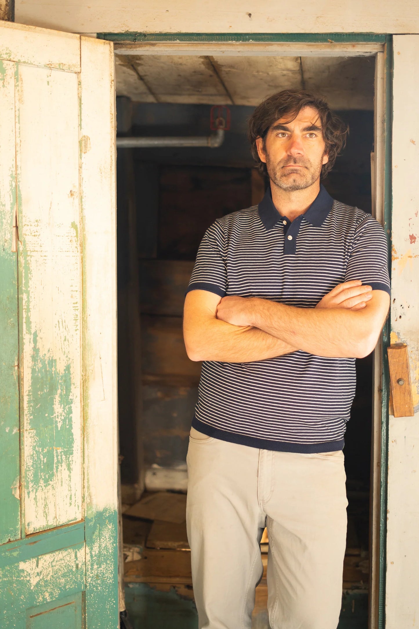 A man standing in a doorway while wearing the Navy SeaWell Striped Knit Polo by Long Wharf Supply