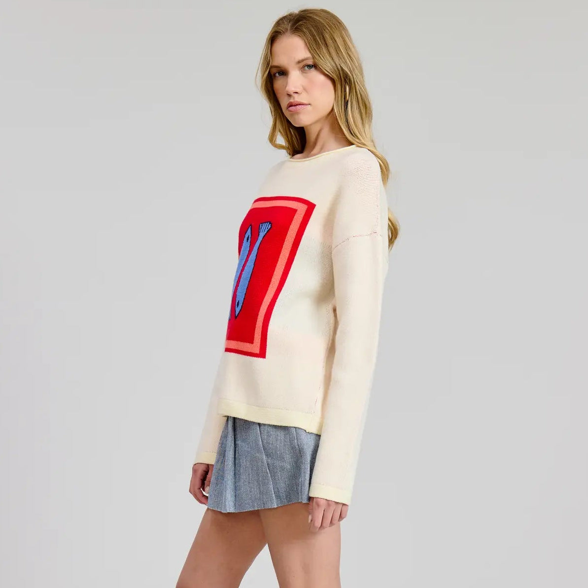 Woman wearing a cream sweater with a colorful sardine design paired with a denim skirt