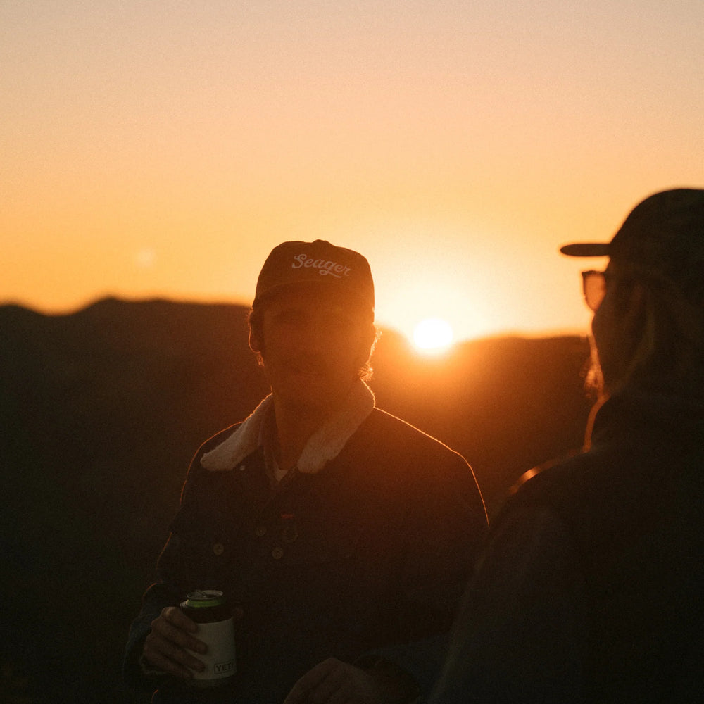 
                      
                        A man drinking with friends as the sun sets. He's wearing the Big Khak Corduroy Snapback Hat by the brand Seager
                      
                    