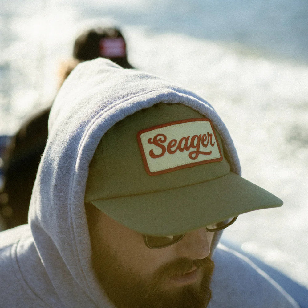 A man wearing the Green Uncle Bill Hemp Snapback Hat by the brand Seager with a hoodie pulled over the top of it.