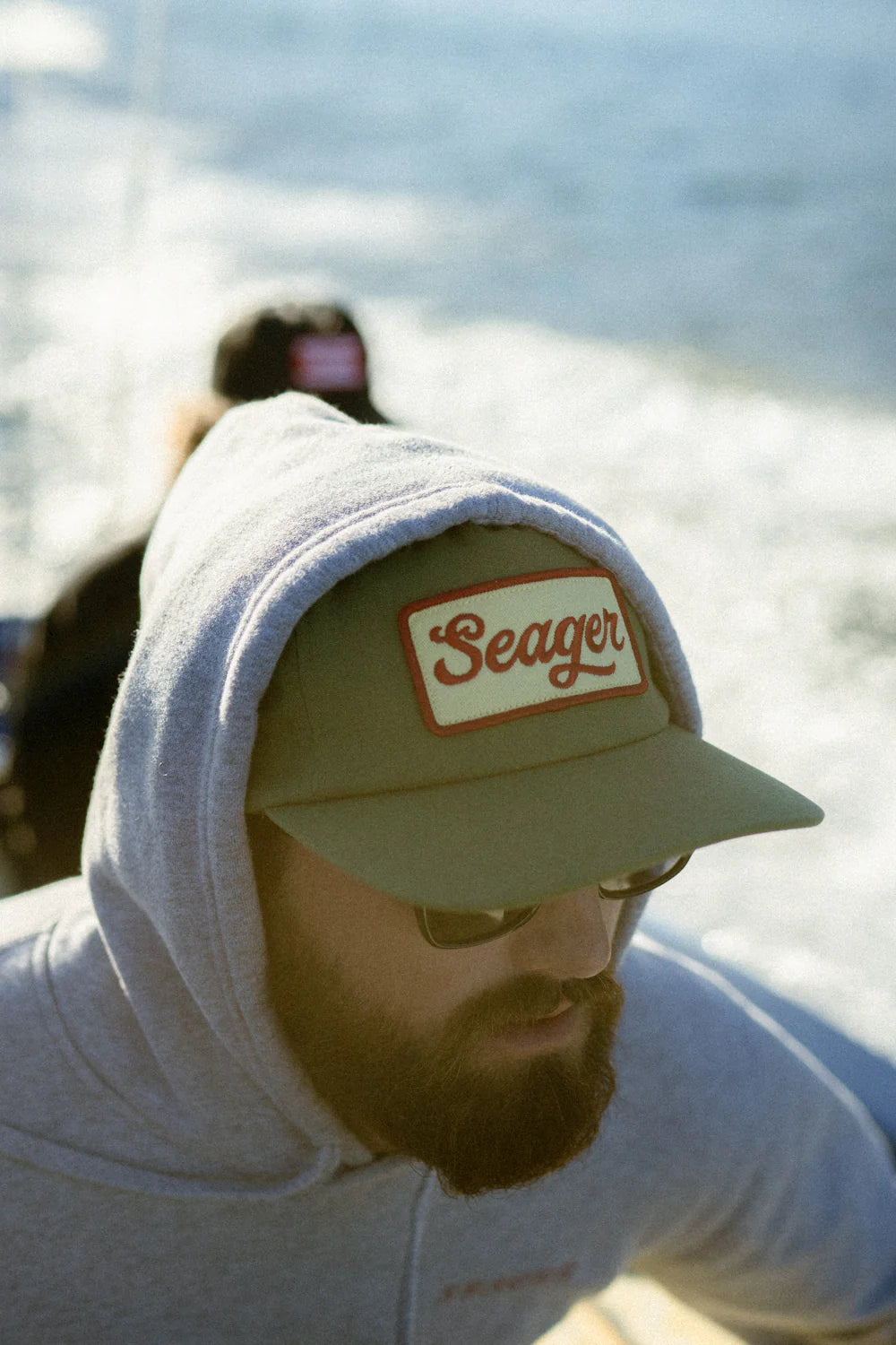 A man wearing the Green Uncle Bill Hemp Snapback Hat by the brand Seager with a hoodie pulled over the top of it.