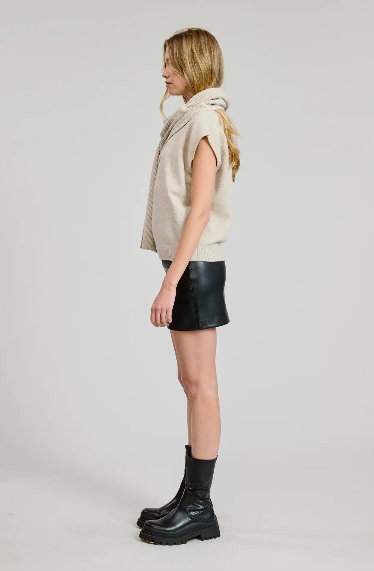 Woman wearing a beige sweater top with a black mini skirt and black boots