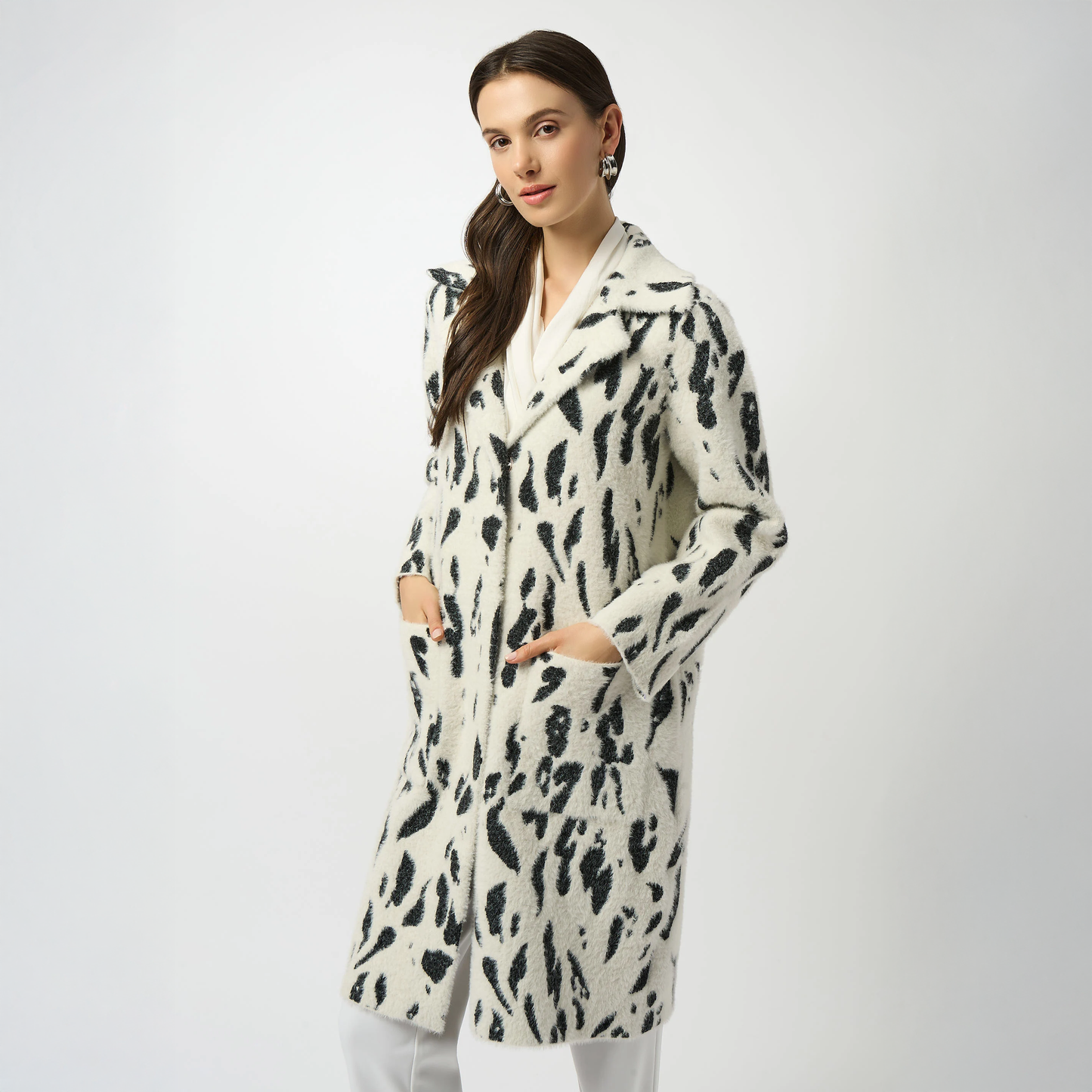 Woman wearing a white coat with black animal print pattern on a plain background. The coat is the Joseph Ribkoff Feather Yarn Animal Jacquard Coat with Faux Fur Trim