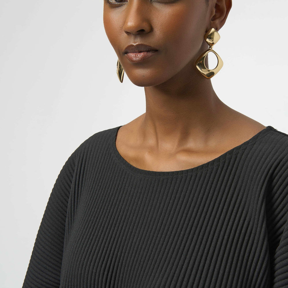 Woman wearing a black scoop neck top with gold hoop earrings 