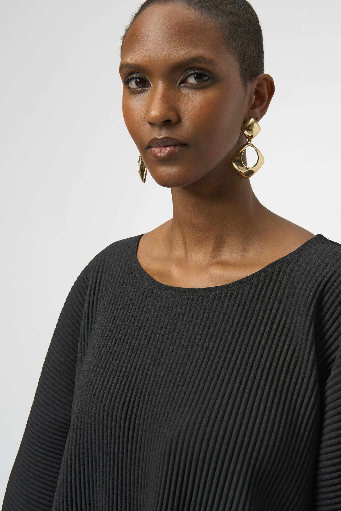 Woman wearing a black scoop neck top with gold hoop earrings 